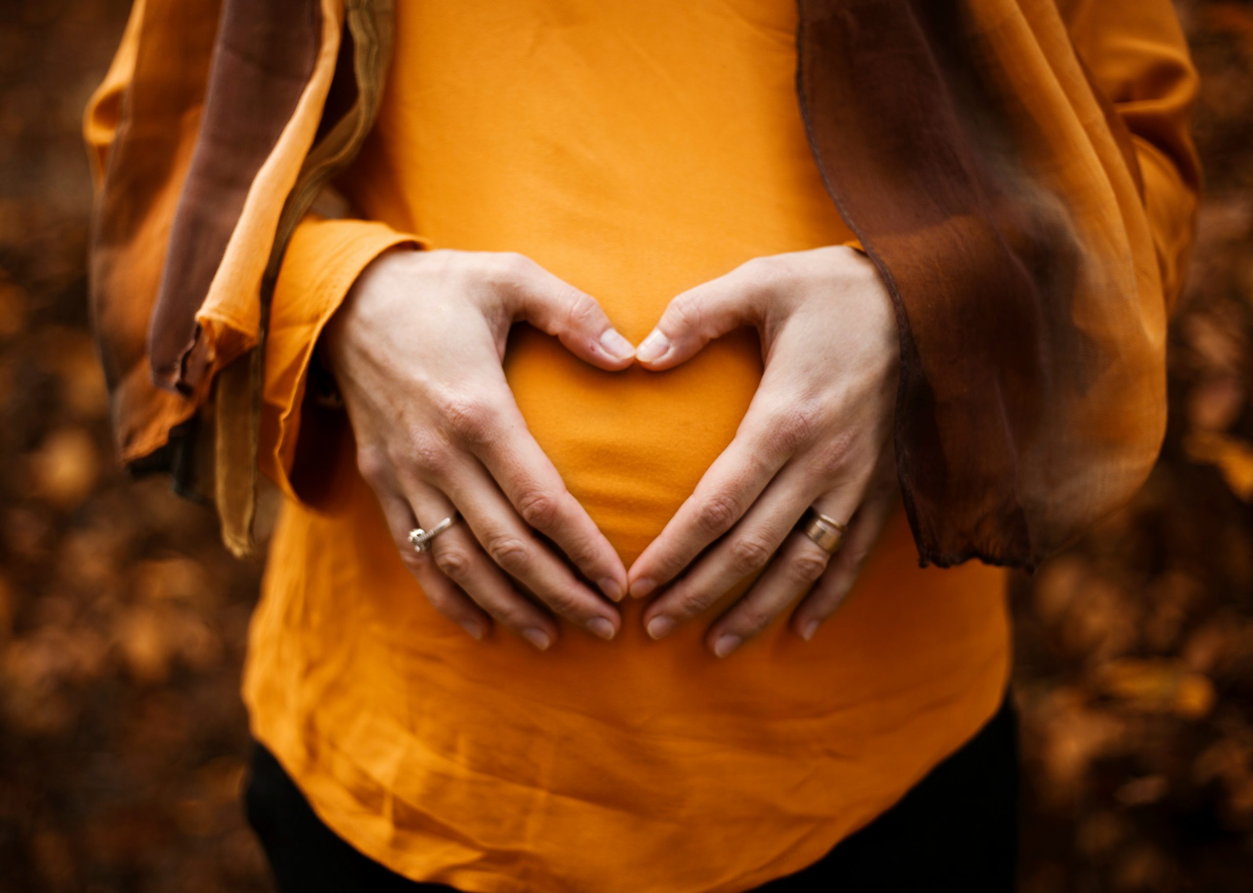 Hands in shape of heart resting on pregnancy bump.